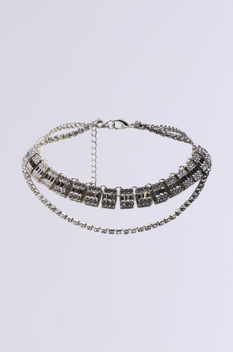 The BLISS NECKLACE SET features a faux silver finish with two strands: an intricate rectangular rhinestone chain and a simple chain, both secured with an adjustable lobster clasp closure, showcased against a plain white background.