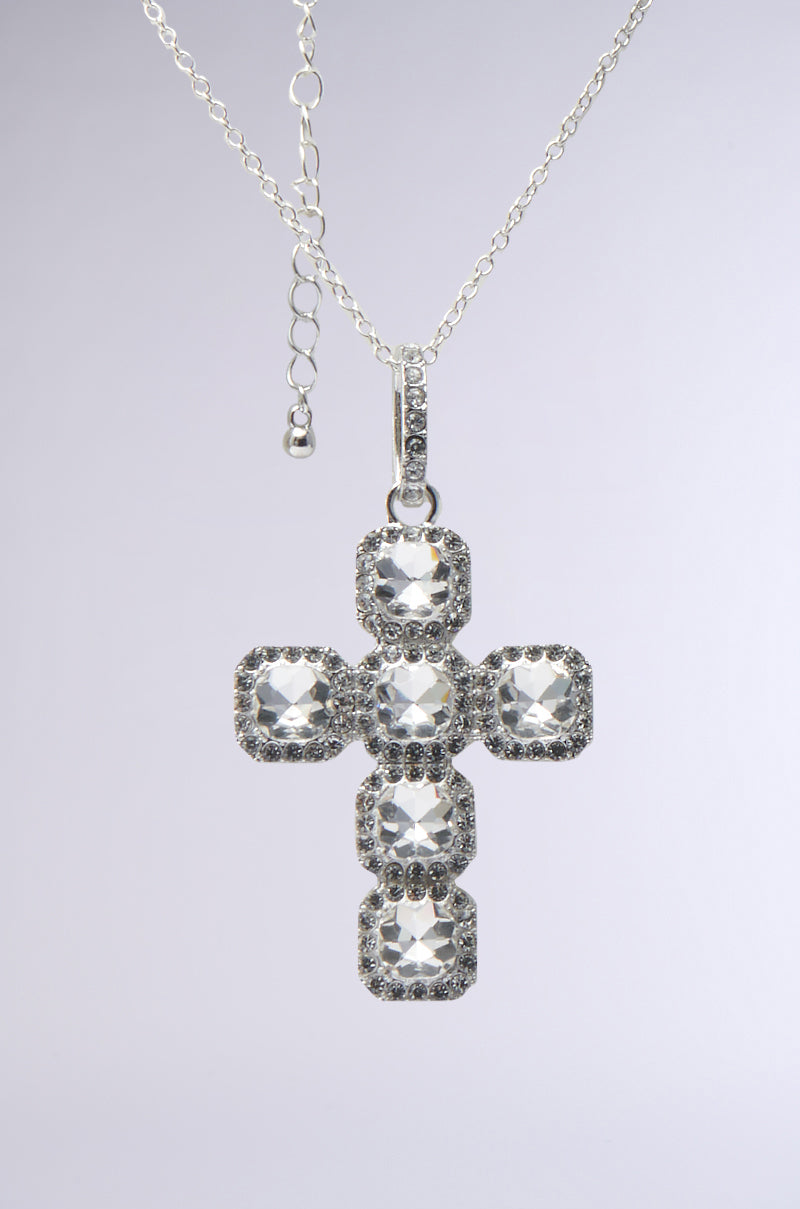 The I AM EVERYTHING SILVER NECKLACE features a striking cross pendant with five large square-cut clear gemstones, surrounded by smaller sparkling stones. It shines elegantly against a plain light background—a true masterpiece.