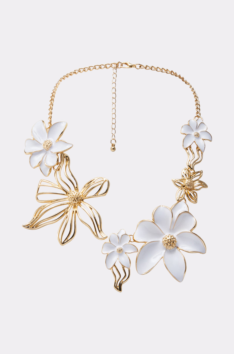 IN THE GARDEN NECKLACE: Gold chain necklace adorned with large, sculpted white and gold flowers featuring intricate petal designs and textured gold centers—a bold floral statement piece on a plain light background.