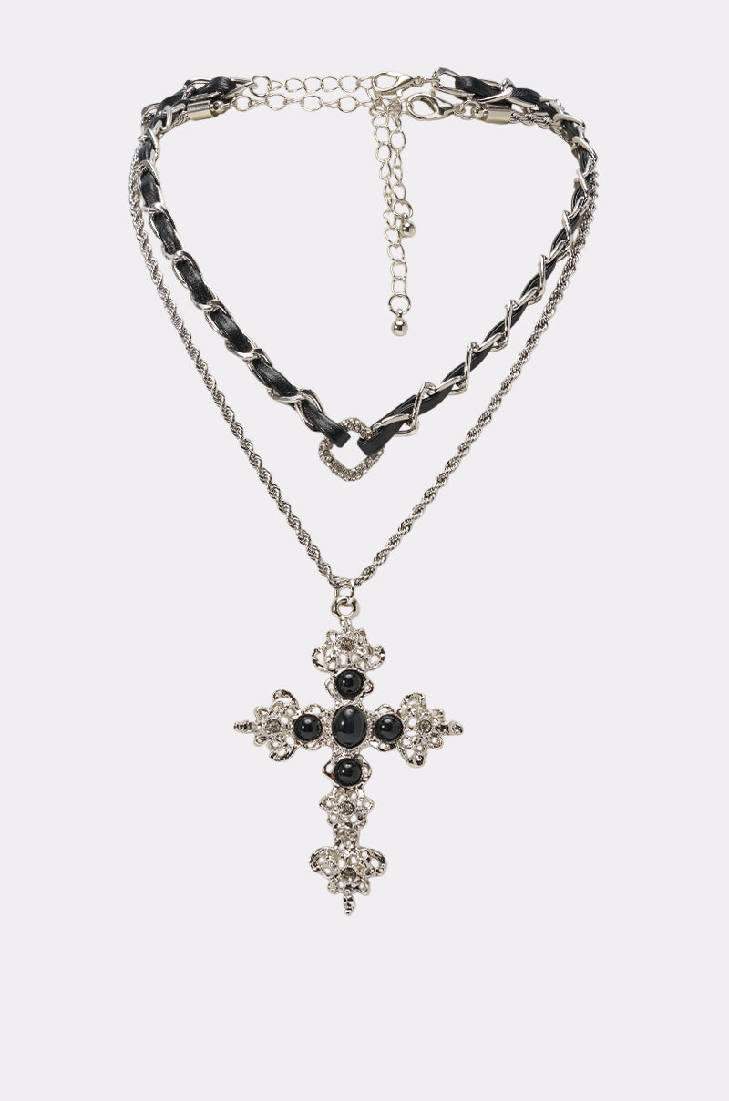 The CROSS MY HEART NECKLACE features a silver chain with black accents and a large ornate cross pendant embellished with black and clear gemstones, shown on a plain white background.