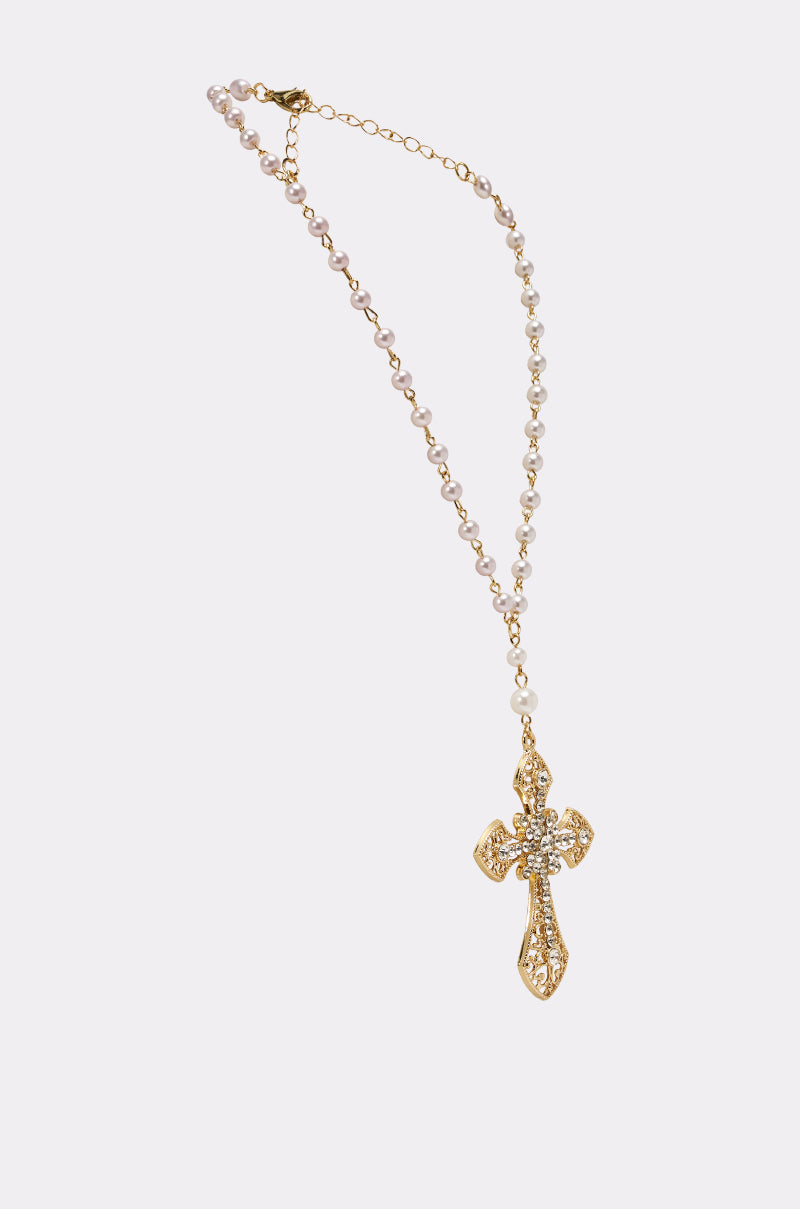 The PRAYERS UP NECKLACE is a gold statement piece featuring small white beads and a large, ornate cross pendant embellished with clear gemstones, shown against a simple white background. 2