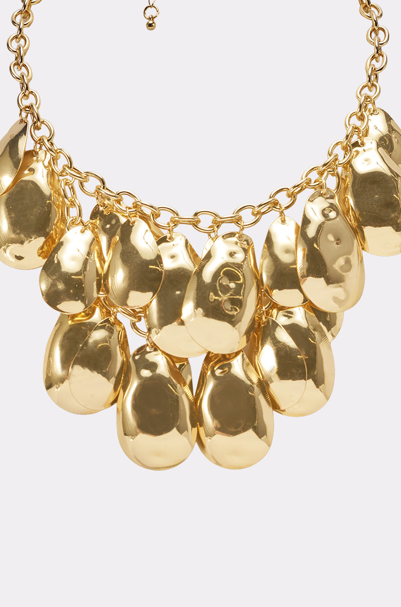The ON A TRIP NECKLACE is a gold choker with several large, shiny hammered teardrop pendants hanging from a chunky curb chain, displayed against a plain light background. 4