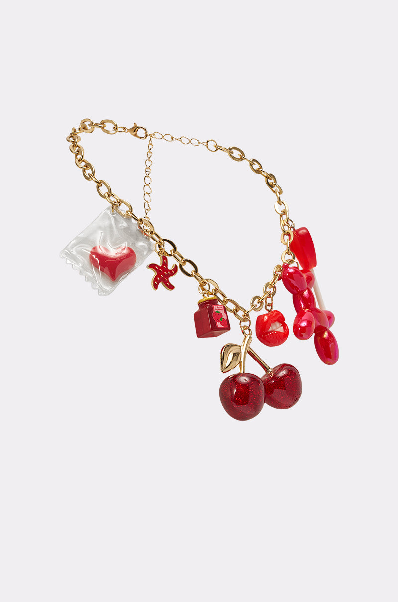 The HAVE SOME FUN NECKLACE features a chunky gold chain with playful red charms—cherries, lips, a starfish, pills, and a pillow-like shape—giving off major Y2K vibes against a light background. 2