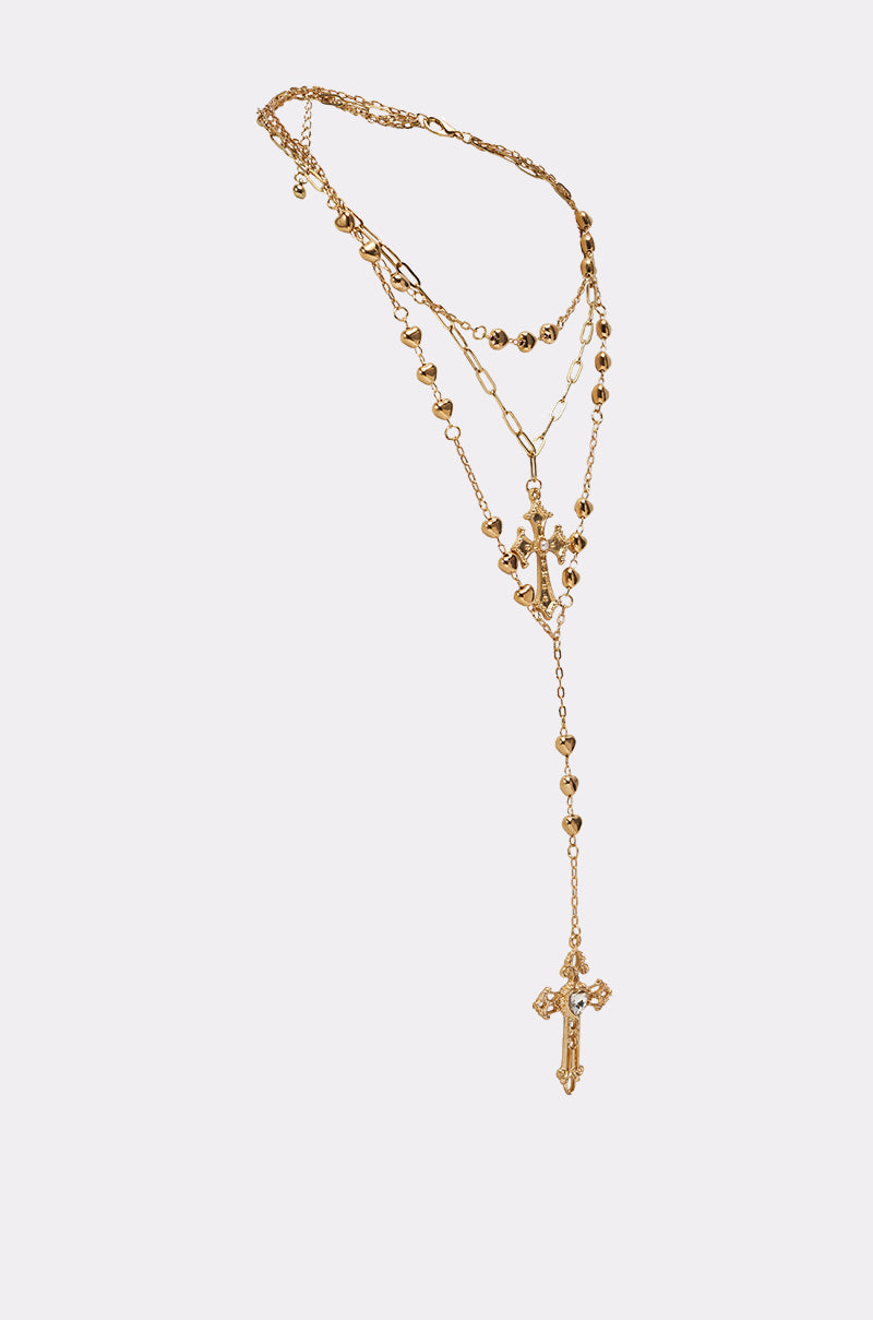 The DRIPPED OUT CROSS LARIAT is a gold-tone layered necklace with delicate chains, small bead details, an ornate "M" charm, and a striking cross lariat finished with a decorative pendant. 2
