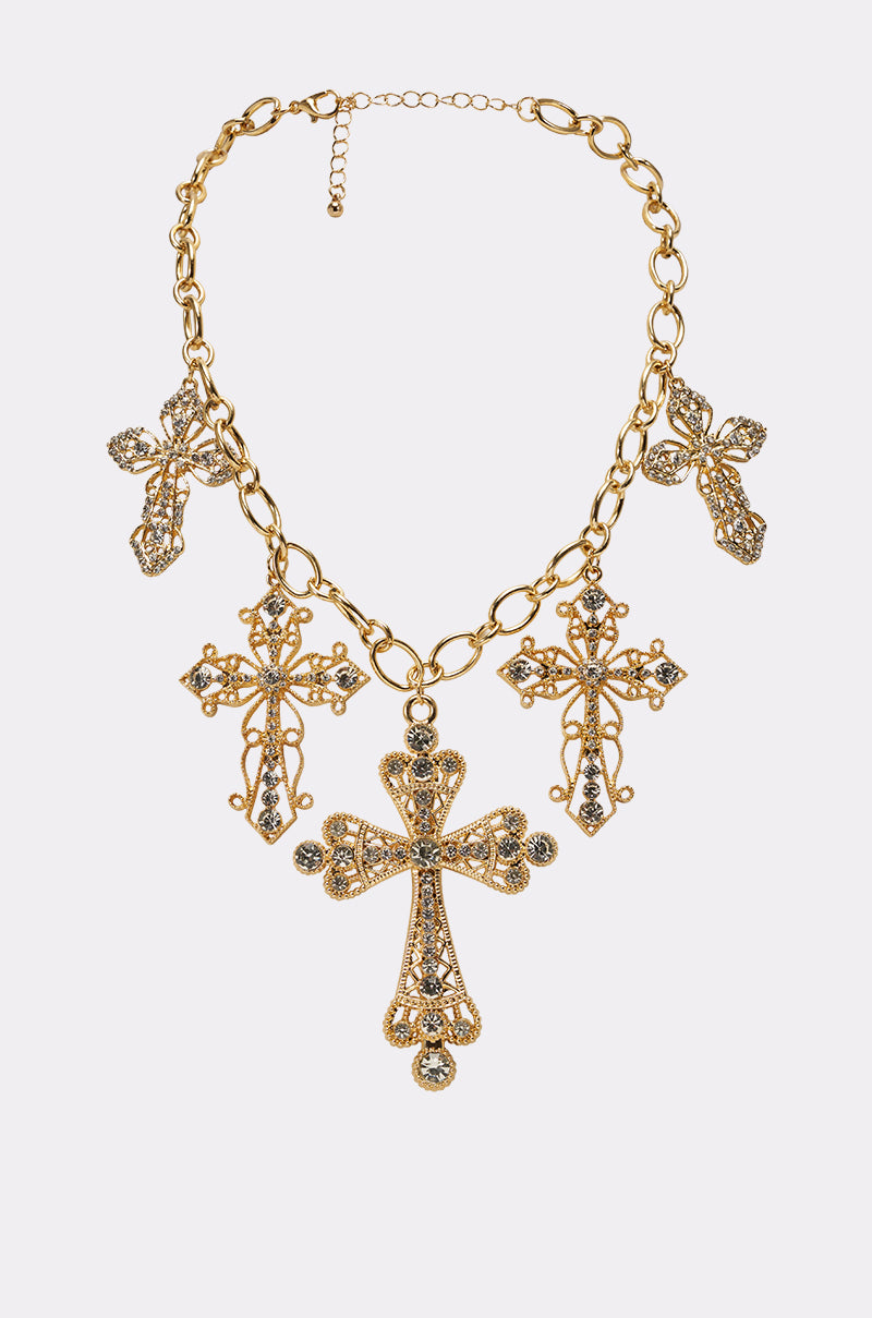 The TAKE A CHANCE NECKLACE is a gold chain with a large central rhinestone cross and four smaller crosses, creating a bold statement piece. Displayed on a plain white background, it's the perfect ornate cross necklace for standout style. 1