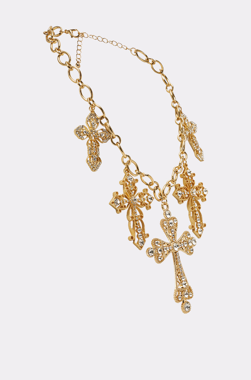 The TAKE A CHANCE NECKLACE is a gold chain featuring five rhinestone cross pendants, each encrusted with sparkling stones, shown on a white background. 3