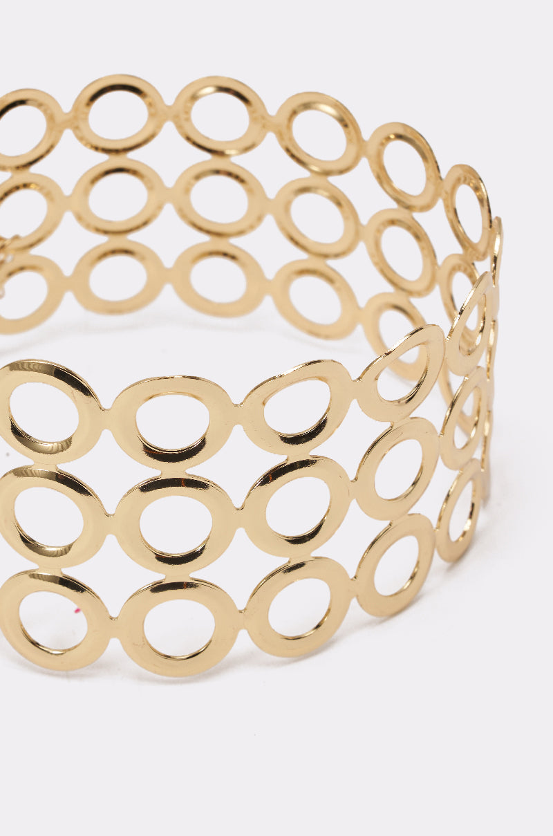 The TITI NECKLACE features a wide gold cuff bracelet with a shiny finish and open oval pattern, offering a geometric, modern look. Pair it with a statement or gold choker necklace for bold, polished style. 5