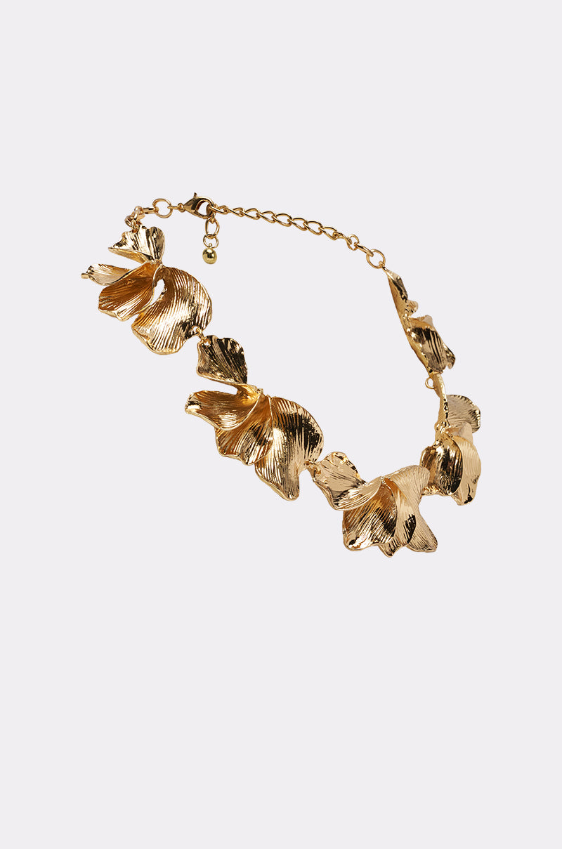 The ON A BEACH NECKLACE is a gold-tone statement piece with five large, textured leaf-shaped pendants featuring intricate detailing and an adjustable chain and clasp, shown on a simple light background. 2