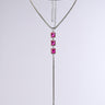 Introducing the NIKKI LONG NECKLACE: a luxury piece featuring a silver choker with an intricate grid design, complemented by a long chain pendant adorned with three large rectangular pink gemstones. The statement accessory's lower portion includes a dangling silver chain, all set against a plain gray background.