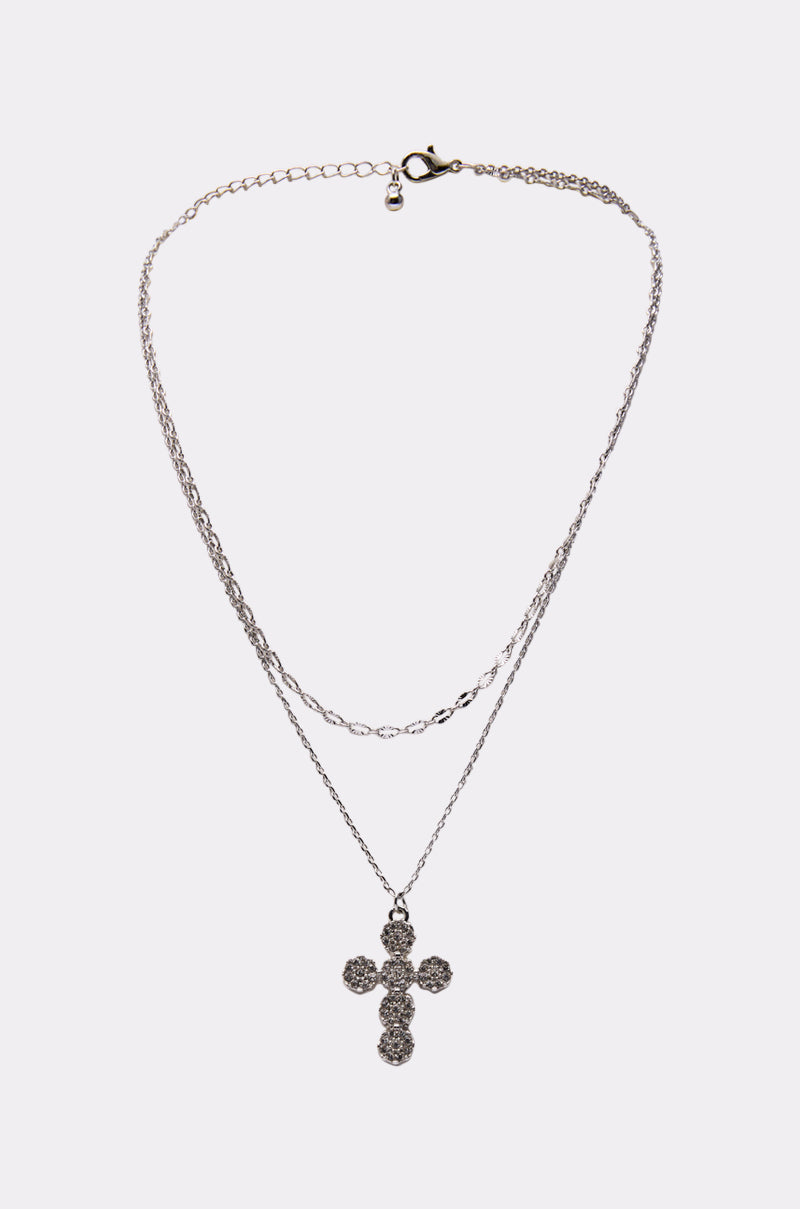 The CROSS NECKLACE features a double-layered silver-tone chain with crystal accents, sparkling beautifully against a plain white background. 1