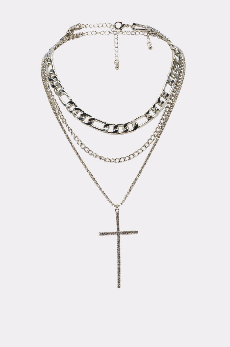The CROSS ME NECKLACE IN SILVER features a chunky chain choker, delicate layered chains, and a long hanging cross, creating a bold and stylish layered necklace set.