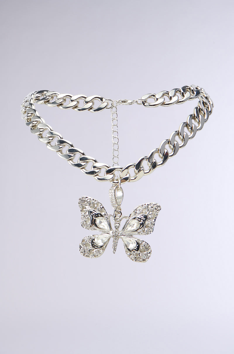 The FLY AWAY PENDANT NECKLACE showcases a chunky silver chain adorned with a butterfly pendant, intricately decorated with rhinestone details. Featuring a lobster clasp closure and an adjustable chain to modify its length, it stands out beautifully against the plain white background.