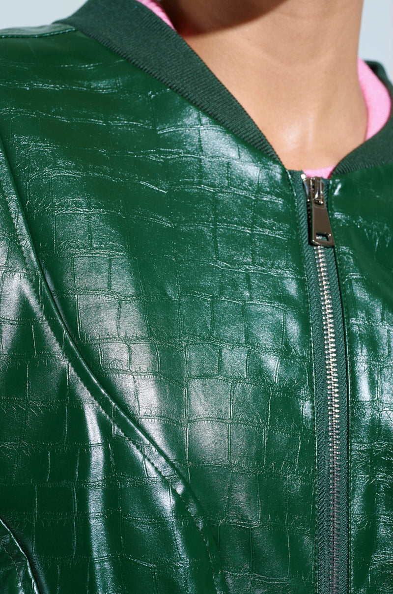 Close-up of YOKON EMBOSSED FAUX LEATHER BOMBER in shiny green, crafted from vegan faux leather with an embossed crocodile pattern. It features a silver front zipper, a dark green collar, and is lined with light pink fabric.