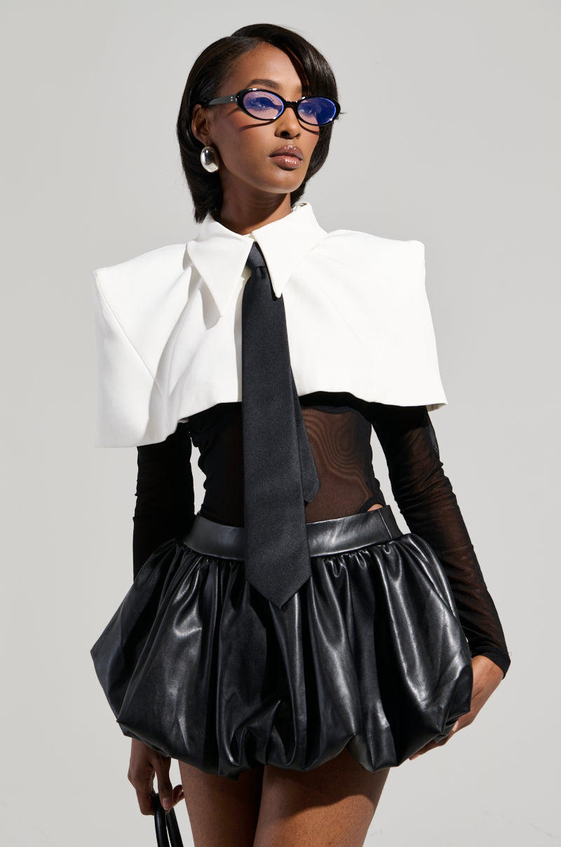 A fashionable person wears the "Reservation At 8 Tie Detail Mesh Long Sleeve Collared Top" paired with a black short leather skirt. Stylish eyewear, black gloves, and pearl earrings complete the look against a plain and neutral background.