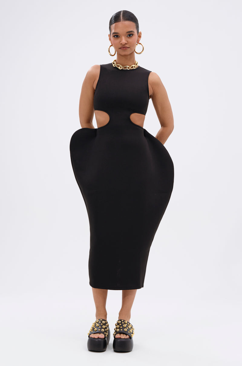 A woman stands against a white background wearing the ONE OF ONE ABSTRACT MIDI DRESS with side cutouts and rounded hip details, styled with gold hoop earrings, a chunky necklace, and platform shoes for an avant-garde look.