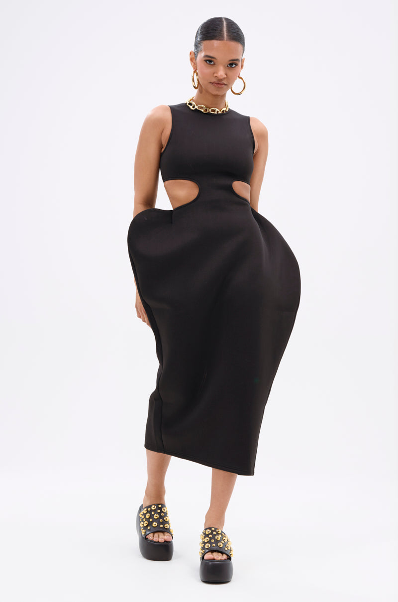 Wearing the ONE OF ONE ABSTRACT MIDI DRESS with side cutouts and a sculpted silhouette, she pairs it with chunky platform sandals, gold stud details, and a thick gold chain necklace for an avant-garde look with sleek, pulled-back hair.