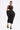 Wearing the ONE OF ONE ABSTRACT MIDI DRESS with side cutouts and a sculpted silhouette, she pairs it with chunky platform sandals, gold stud details, and a thick gold chain necklace for an avant-garde look with sleek, pulled-back hair.