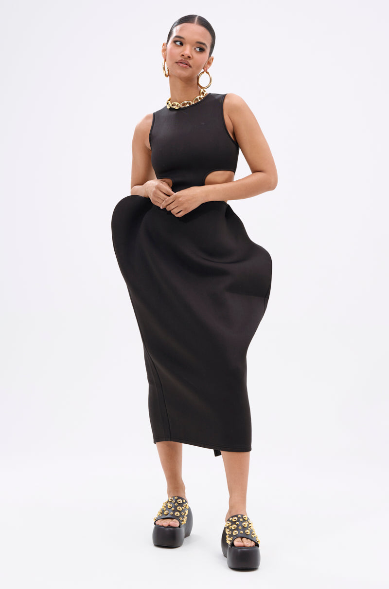 A woman wears the ONE OF ONE ABSTRACT MIDI DRESS, a sleeveless black midi with waist cutouts and sculpted hips. She completes the sculptural look with gold hoop earrings, a chunky necklace, and embellished platform sandals.