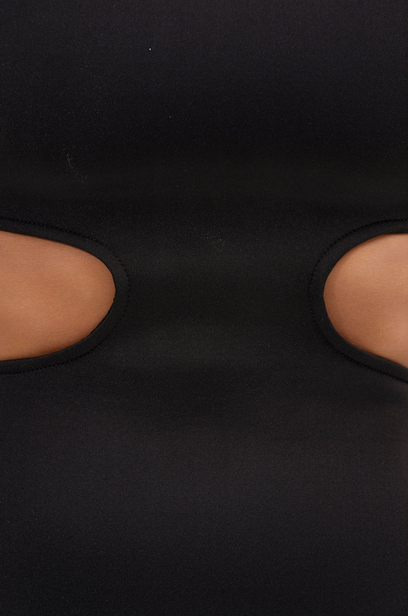 A close-up of black fabric from the ONE OF ONE ABSTRACT MIDI DRESS shows two oval cutouts revealing a tan surface, highlighting its smooth, stretchy texture and sculptural, avant-garde design.
