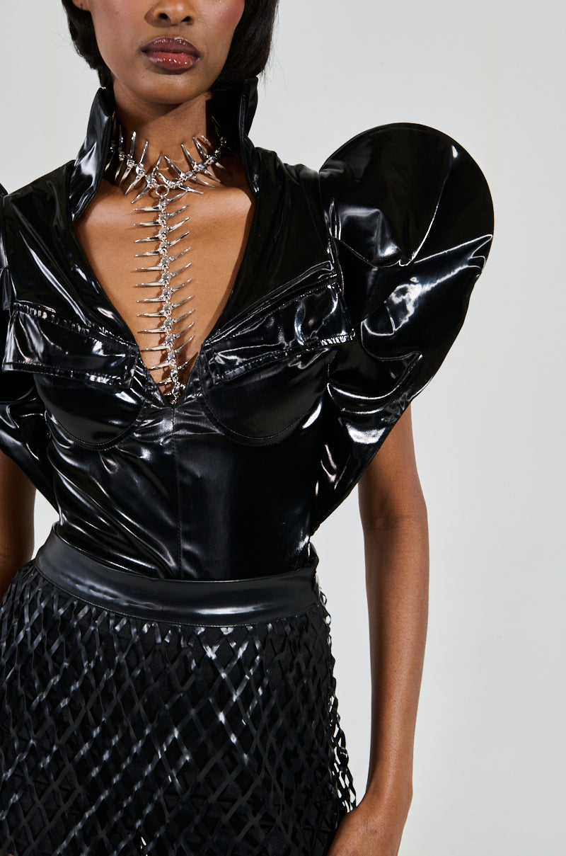 Someone wearing the Veronica Dramatic Shoulder Collared Bodysuit, featuring a black faux leather top with bold shoulders and a plunging neckline accented by metallic details, paired with a skirt showcasing a textured lattice pattern for a striking modern appearance. 7