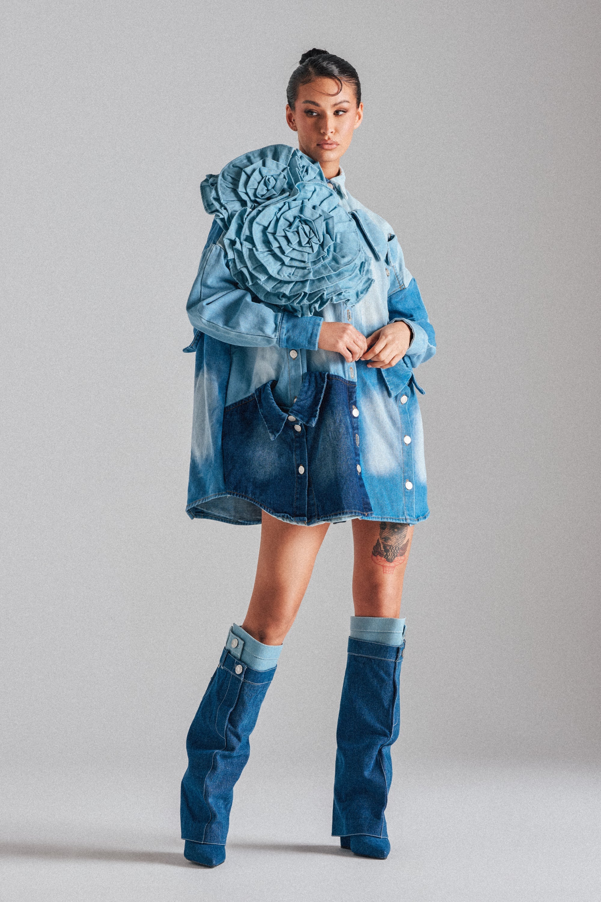 Wearing the SO FINE DENIM BROOCH, a woman exudes confidence in a sky blue denim outfit with oversized ruffled florals, a skirt, and matching boots, posing against a light gray background. 4
