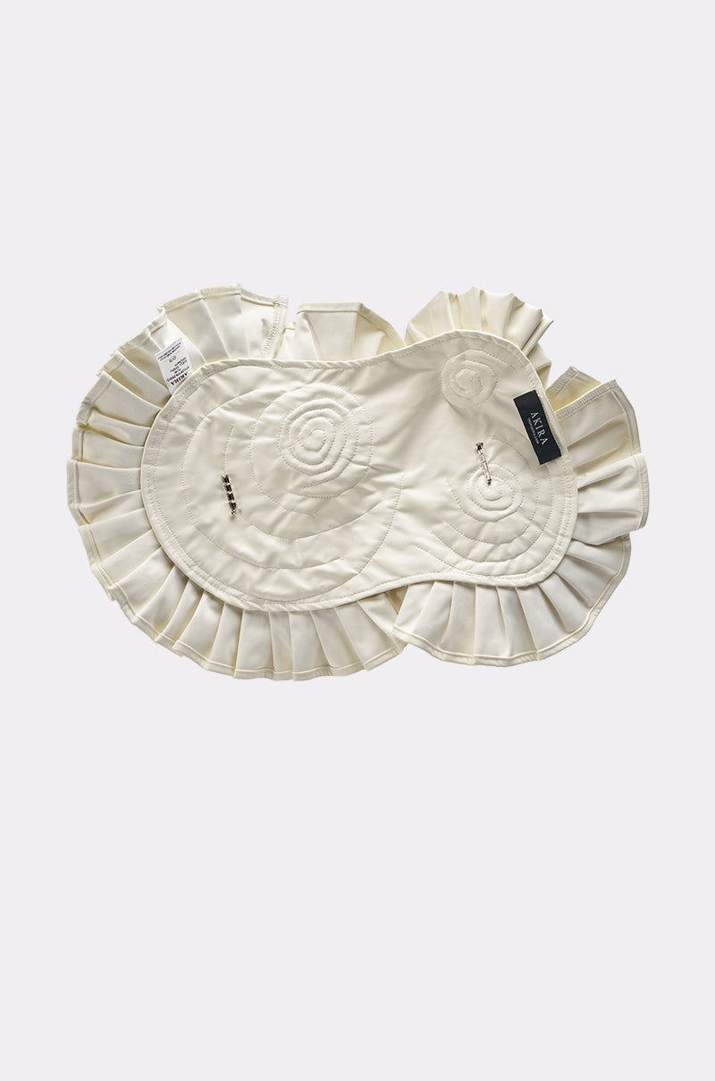 The BLOOMING PU OVERSIZED BROOCH, a cream-toned accessory with ruffle edges, circular quilted patterns, and pleated trim, is shown flat on a light background with a modern faux leather brooch and attached clothing tags. 5