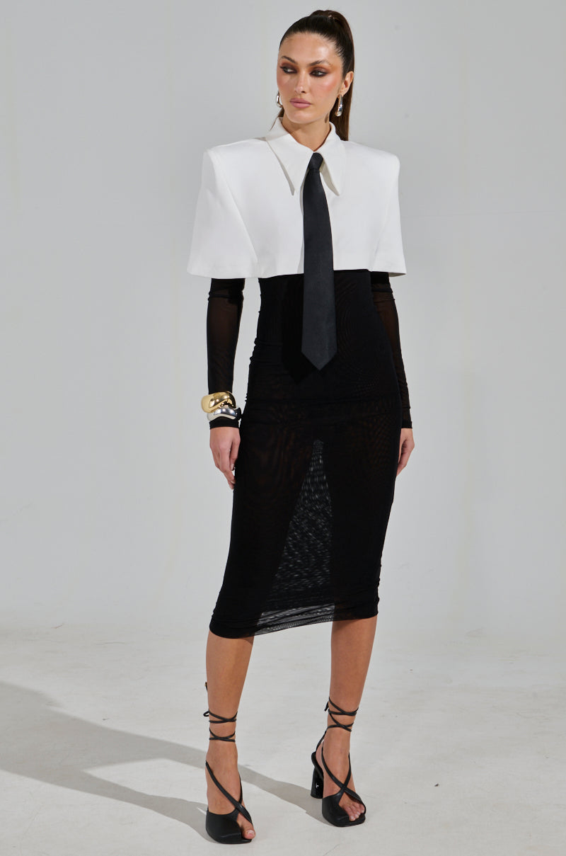 A woman exudes sophistication in the "She Means Business Tie Detail Mesh Midi Dress" paired with a white cape. Gold bracelets and black strappy heels complement her look, while her high ponytail enhances her commanding presence against a plain white background.