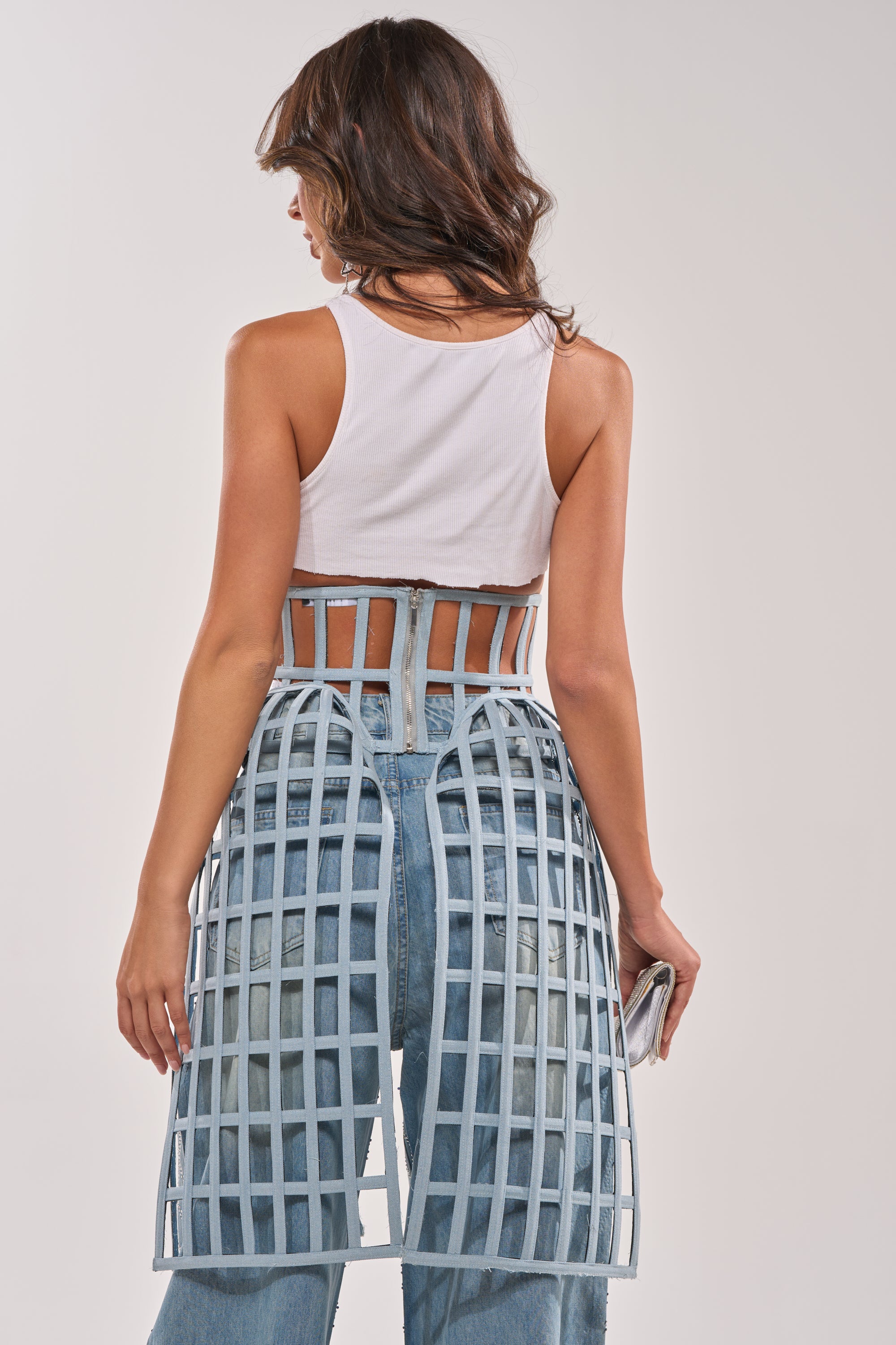 A woman in a white tank top and blue jeans, styled with the NEVER CAGED BELT for an avant-garde touch. 4