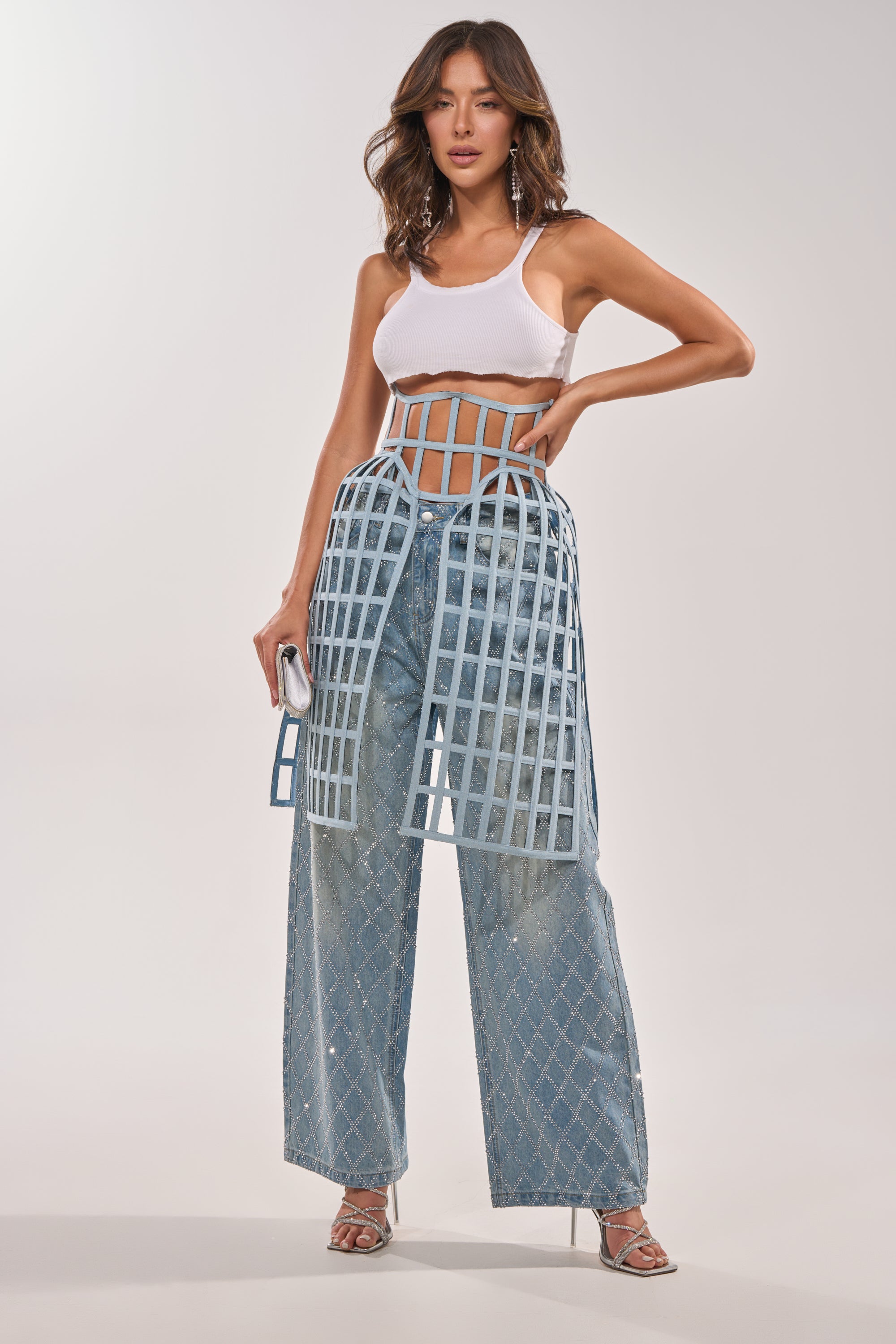 Wearing a white crop top, high-waisted diamond-pattern blue jeans, and the bold NEVER CAGED BELT, she poses confidently with one hand on her hip and heels on her feet. 5