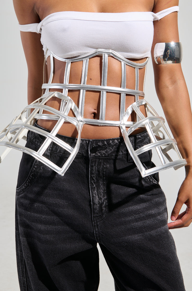 A person is wearing the ULTIMATE TEASE METALLIC CAGE BELT over a white tube top with a cropped fit, paired with black pants. They have a metallic arm cuff on their left arm, and their midriff is exposed, embodying a futuristic and fashion-forward style.