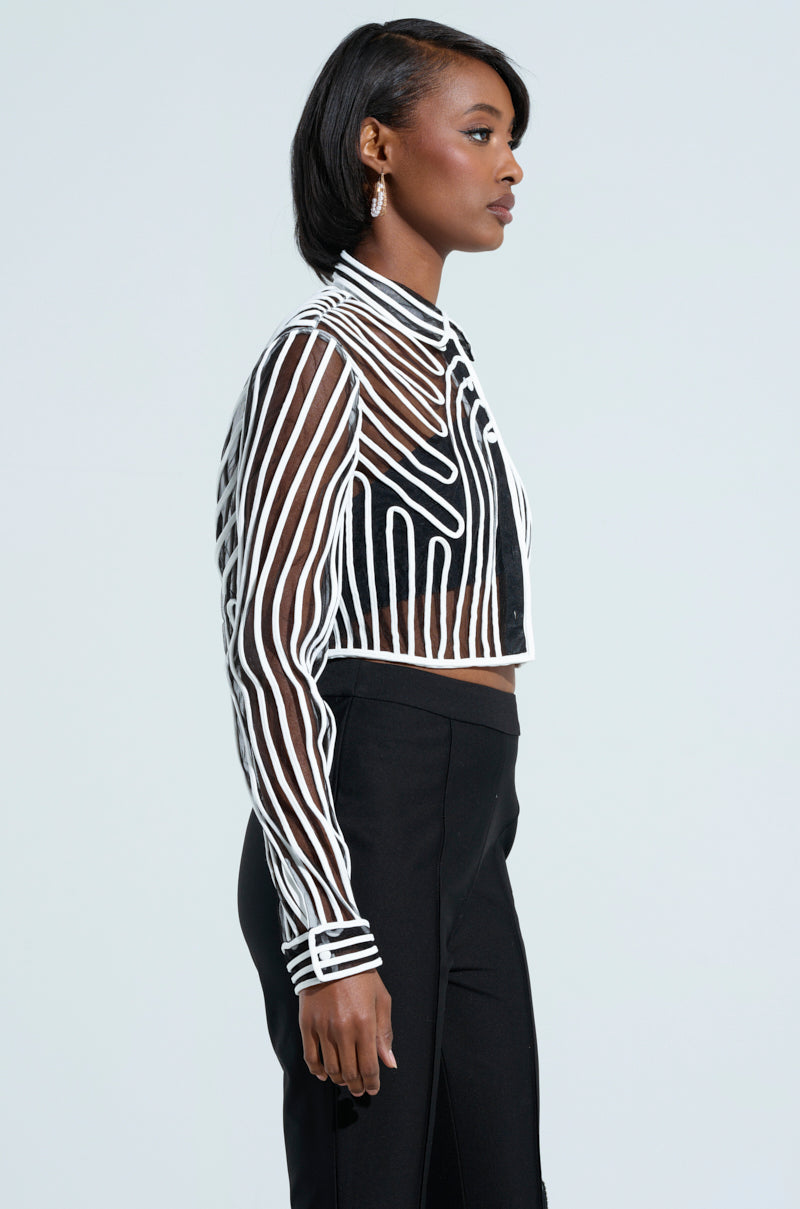 A person is standing in profile against a plain background, wearing the EVA Long Sleeve Button Down Striped Shirt. They have short black hair and are dressed in high-waisted black pants, accentuating the cropped silhouette.