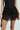 Person wearing a black Spirited Away Skirt with intricate patterns over sheer layers paired with a black top. The skirt boasts layered loops for a textured and elegant look, complemented by a small black handbag in hand.