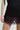 A person wears a SPIRITED AWAY SKIRT featuring intricate loops, paired with a fitted black top. The high-rise silhouette has semi-transparent sections that reveal hints of skin, while the plain background accentuates the outfit's design.