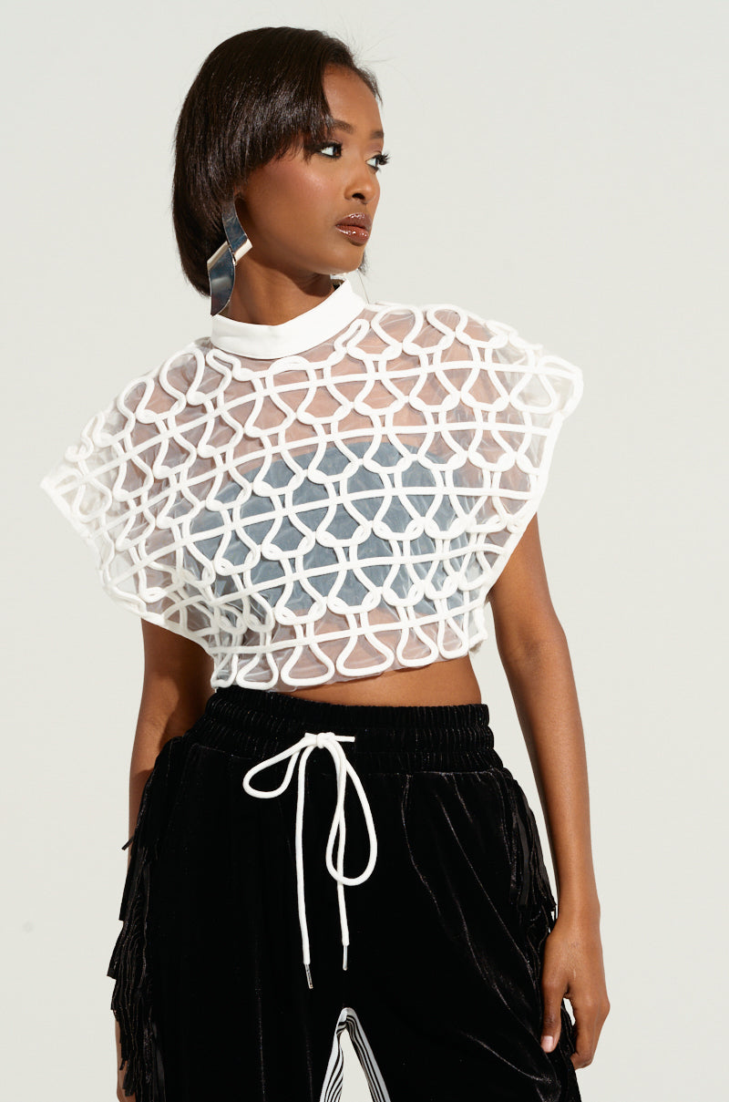 A person with medium-length dark hair is wearing the PURE BLISS TOP—a sleeveless design featuring a sheer white geometric pattern—over a black outfit with a white drawstring. They are looking to the side, standing against a plain background, and sporting large metallic earrings.