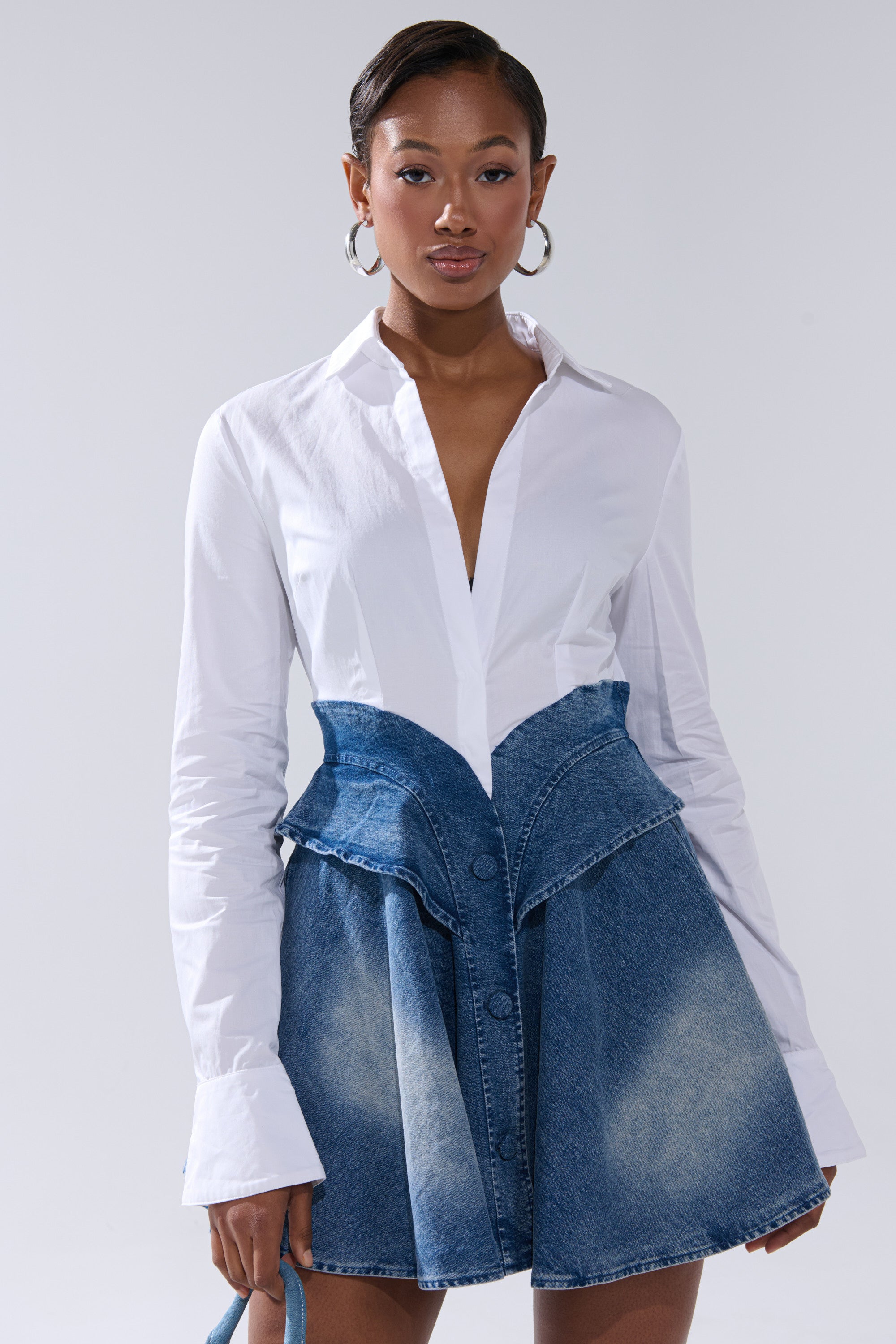 A woman poses confidently in the DONT NEED NOBODY DENIM MINI DRESS against a plain background, accessorized with hoop earrings and sleek hair.