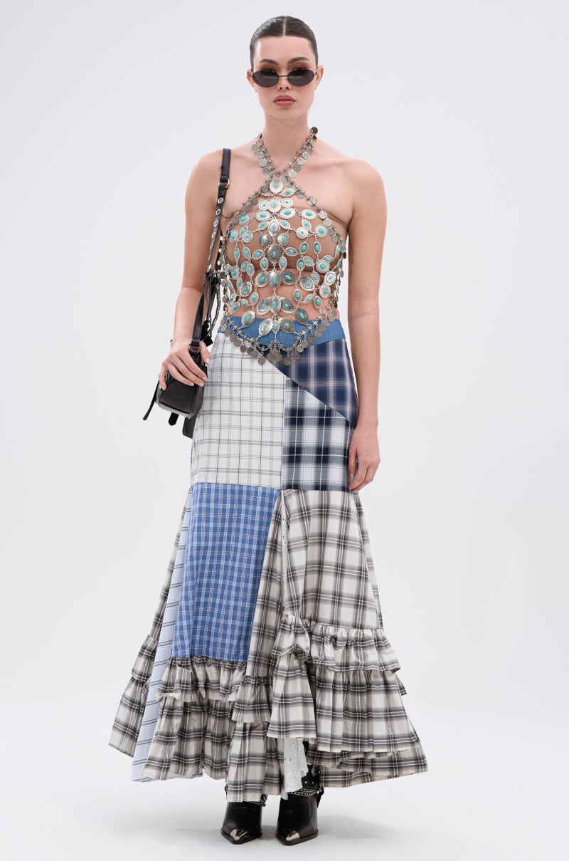 A woman wears sunglasses and the HIGH END RODEO TURQUOISE STONE TOP—a vintage-inspired halter top with metallic discs—paired with a long patchwork plaid skirt, black pointed boots, and a black handbag.