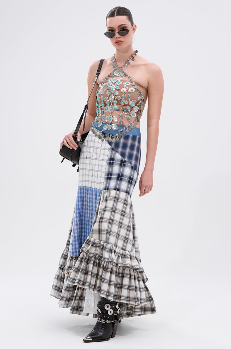 A woman wearing sunglasses, the HIGH END RODEO TURQUOISE STONE TOP with circular metal embellishments, a patchwork plaid maxi skirt with ruffles, studded ankle boots, and a black shoulder bag stands against a white background.