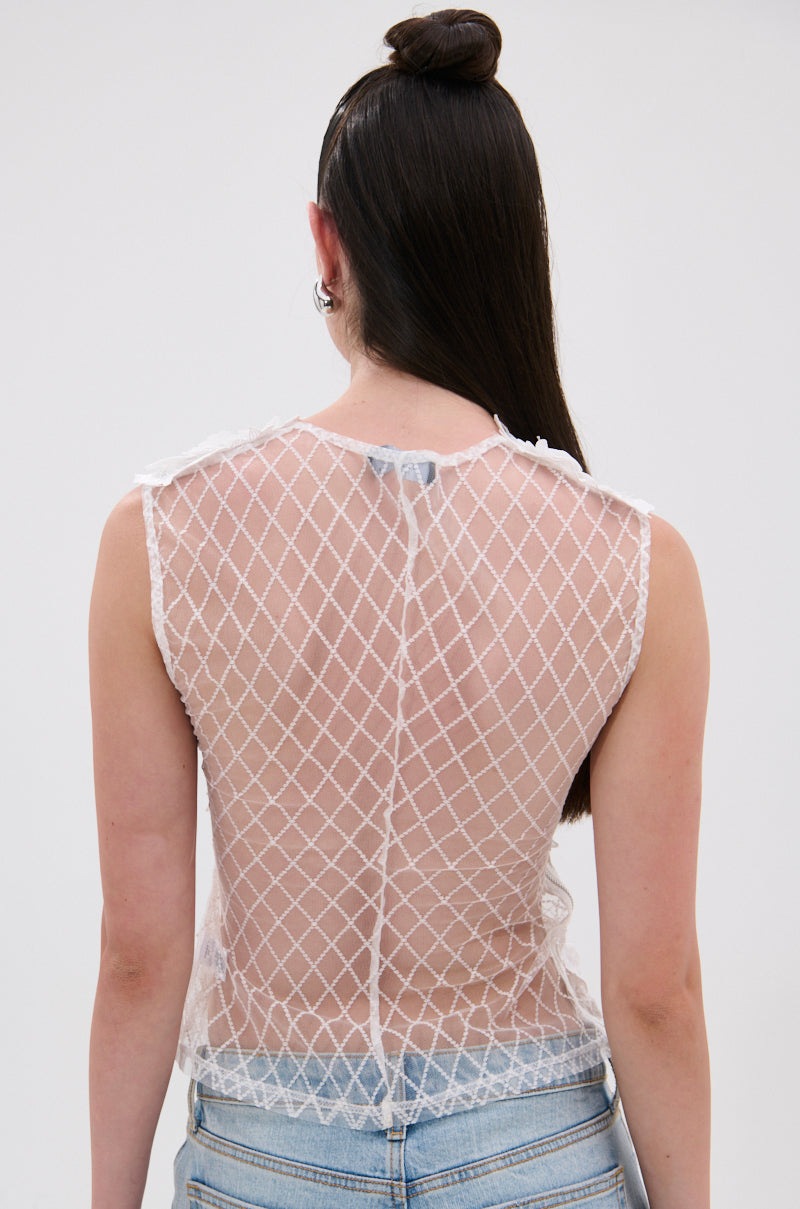 A person with long, straight brown hair in a top knot wears the UNTAMED FLORAL LACE TOP with light blue jeans. The photo, taken from behind against a plain background, highlights the sleeveless sheer mesh design. 3