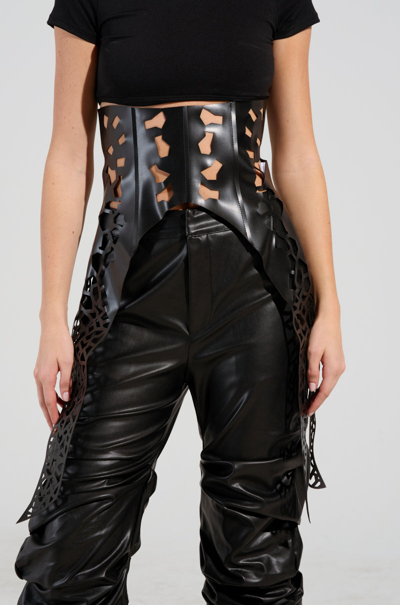 A person is wearing a sleek black cropped top paired with faux leather pants adorned with intricate geometric cut-outs, all accentuated by the SUPERSTAR LASER CUT PU BELT. The ensemble showcases bold patterns as the individual's arms hang naturally by their sides against a simple backdrop.