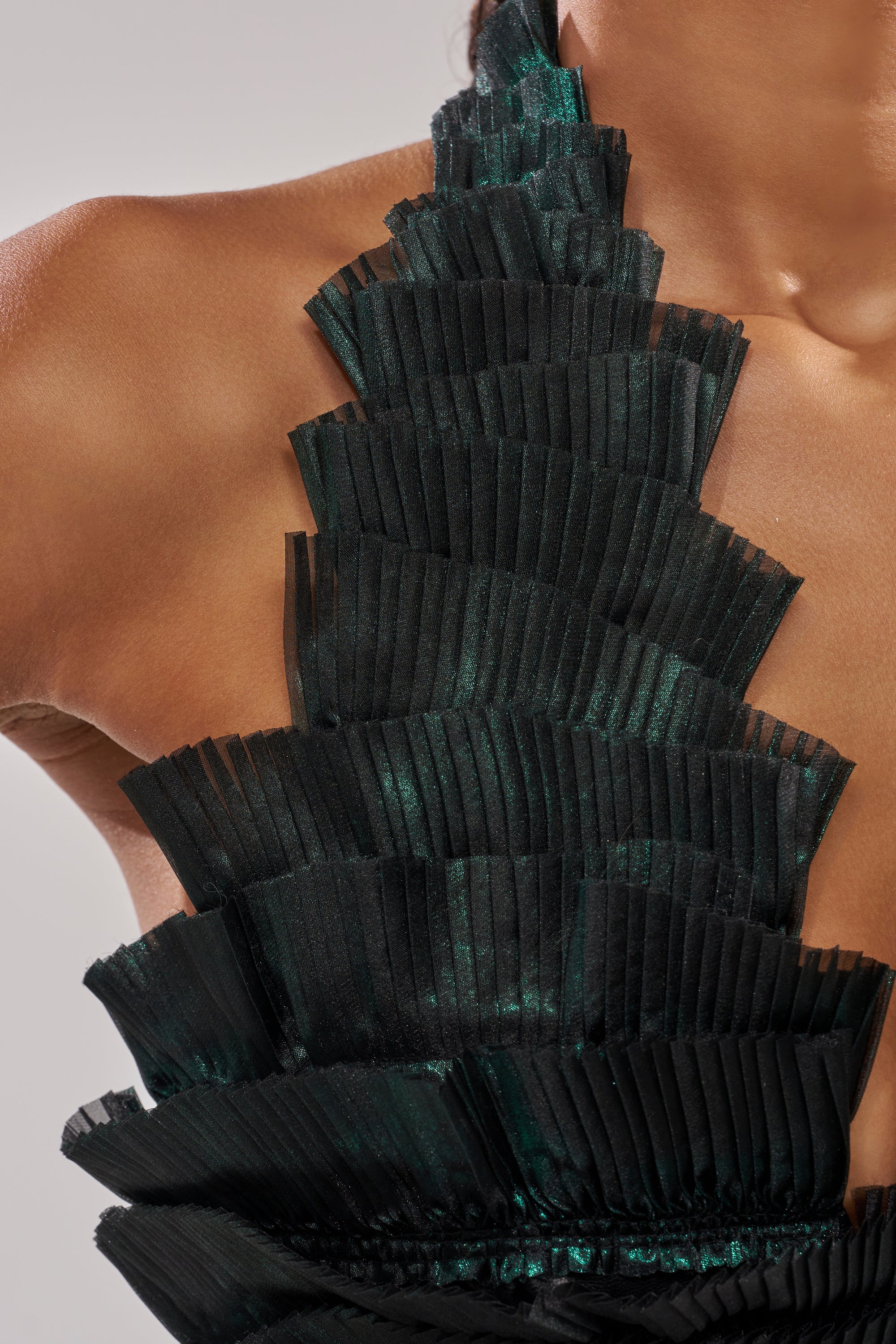 Close-up of a person wearing the DREAMERS HALTER BLOUSE, a unique black organza top with layered, pleated, fan-like textures and a glossy finish draping over the chest and shoulder.