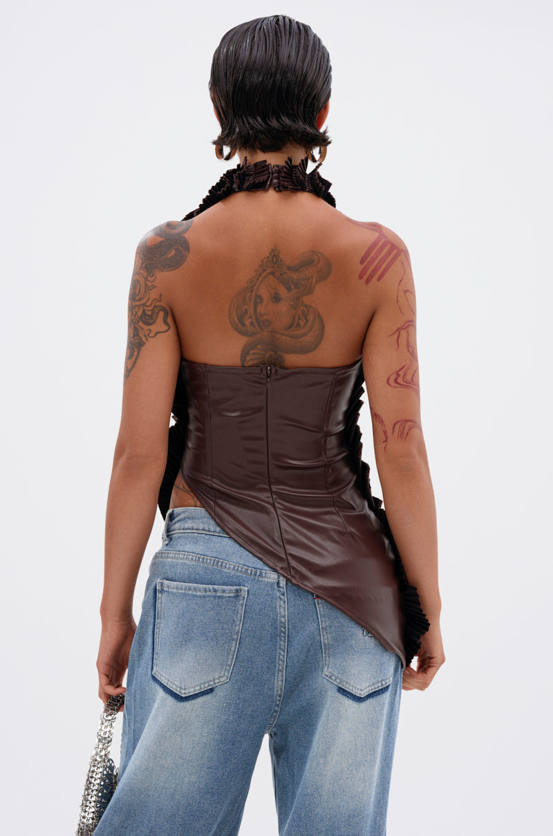 Seen from behind, a person with short, slicked-back hair wears the DREAMERS BLOUSE—a brown faux leather top with an asymmetrical halter neckline—paired with loose blue jeans. Their tattooed back and arms are streaked with red paint as they hold a silver chain bag.