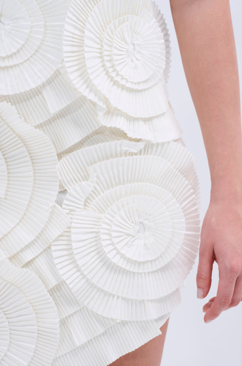 A close-up of a person wearing the ONE OF ONE BANDAGE MINI DRESS IN WHITE; their right arm is visible beside the dress’s sculptural, layered elegance.