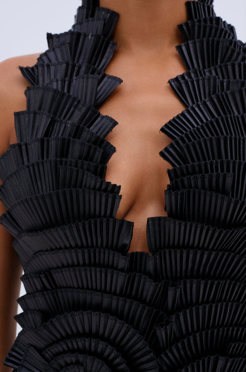 Close-up of a person wearing the ONE OF ONE MINI DRESS IN PU, a sleeveless black faux leather dress with a deep V neckline and layered pleated ruffles in a geometric pattern on the bodice.
