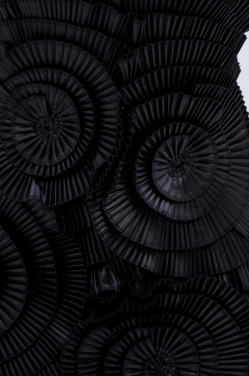 Close-up of overlapping black PU fabric from the ONE OF ONE MINI DRESS arranged in circular, pleated rosettes, creating a textured and visually striking abstract design.