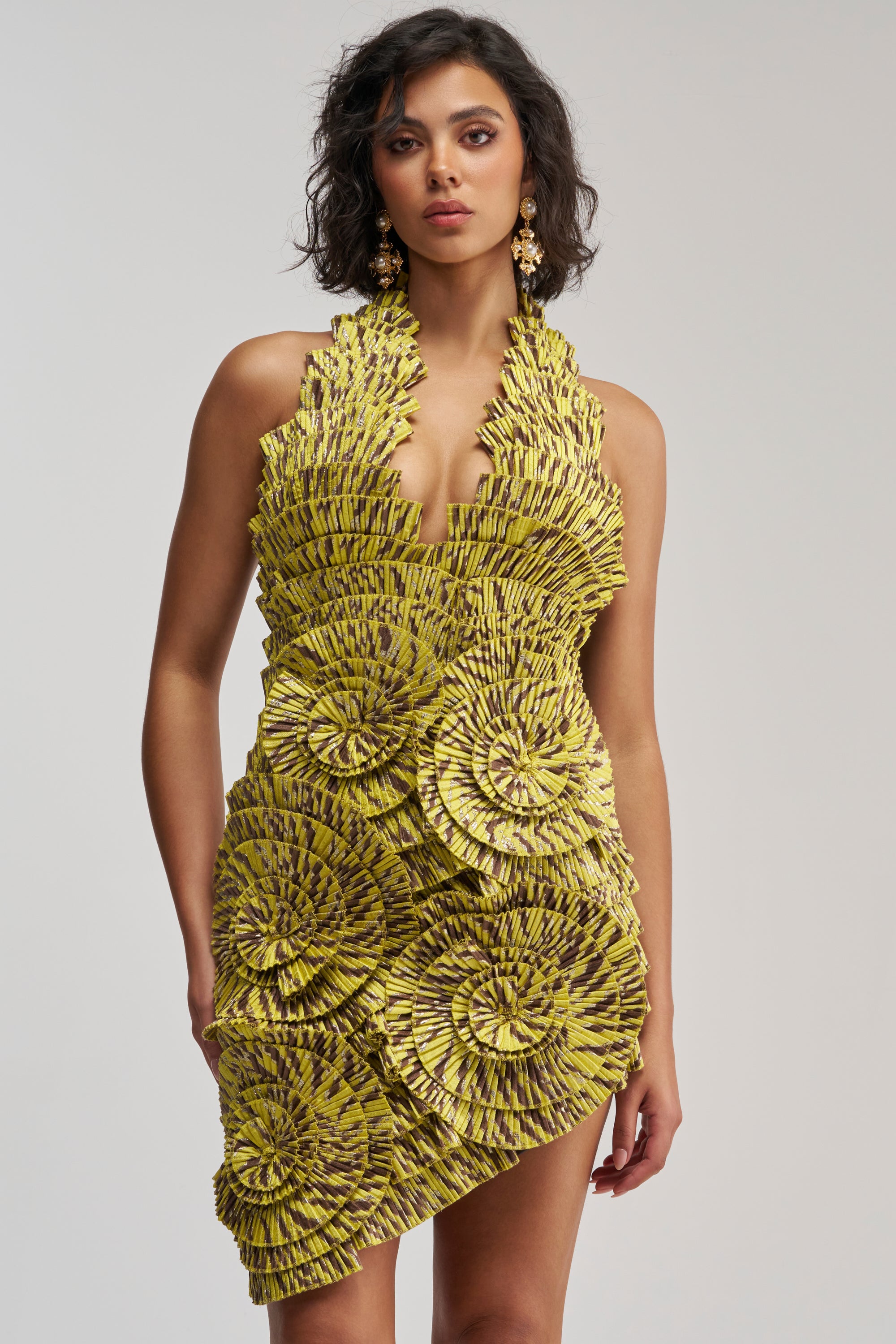 Model showcasing the SHOWING OFF NOVELTY MINI DRESS IN YELLOW MULTI, a yellow pleated halter dress adorned with black textured, layered fan-like circular patterns, posing elegantly against a plain light background.