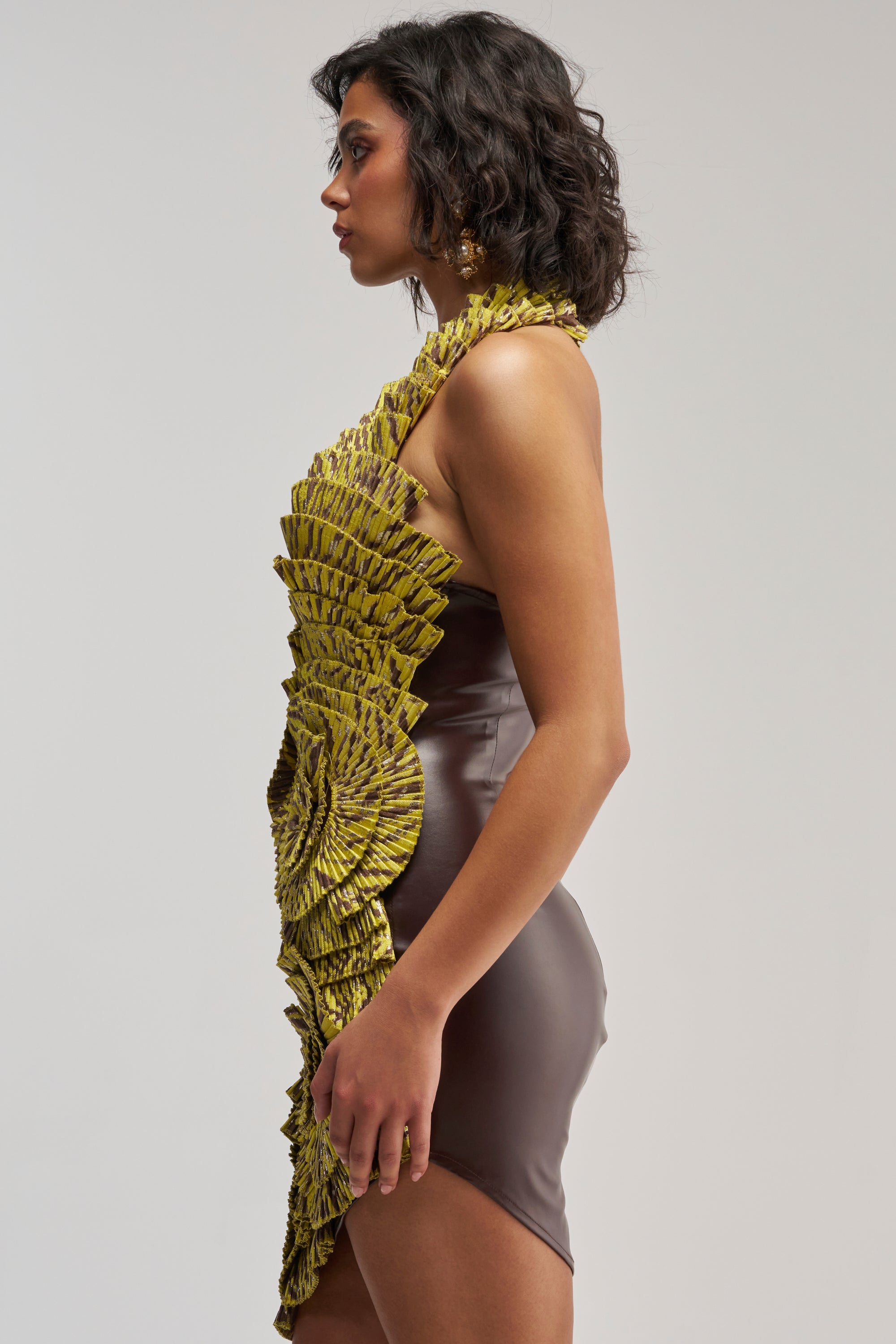 A woman in profile wears the SHOWING OFF NOVELTY MINI DRESS IN YELLOW MULTI, a sleeveless, form-fitting mini dress featuring a brown base adorned with intricate yellow textured ruffles cascading from shoulder to hem, capturing the sophisticated allure of a cocktail party style against a plain background.