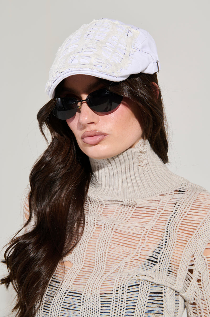 Woman with long brown hair wearing a SPREAD THE NEWS TEXTURED CAP, black sunglasses, and a beige mesh turtleneck top. 1