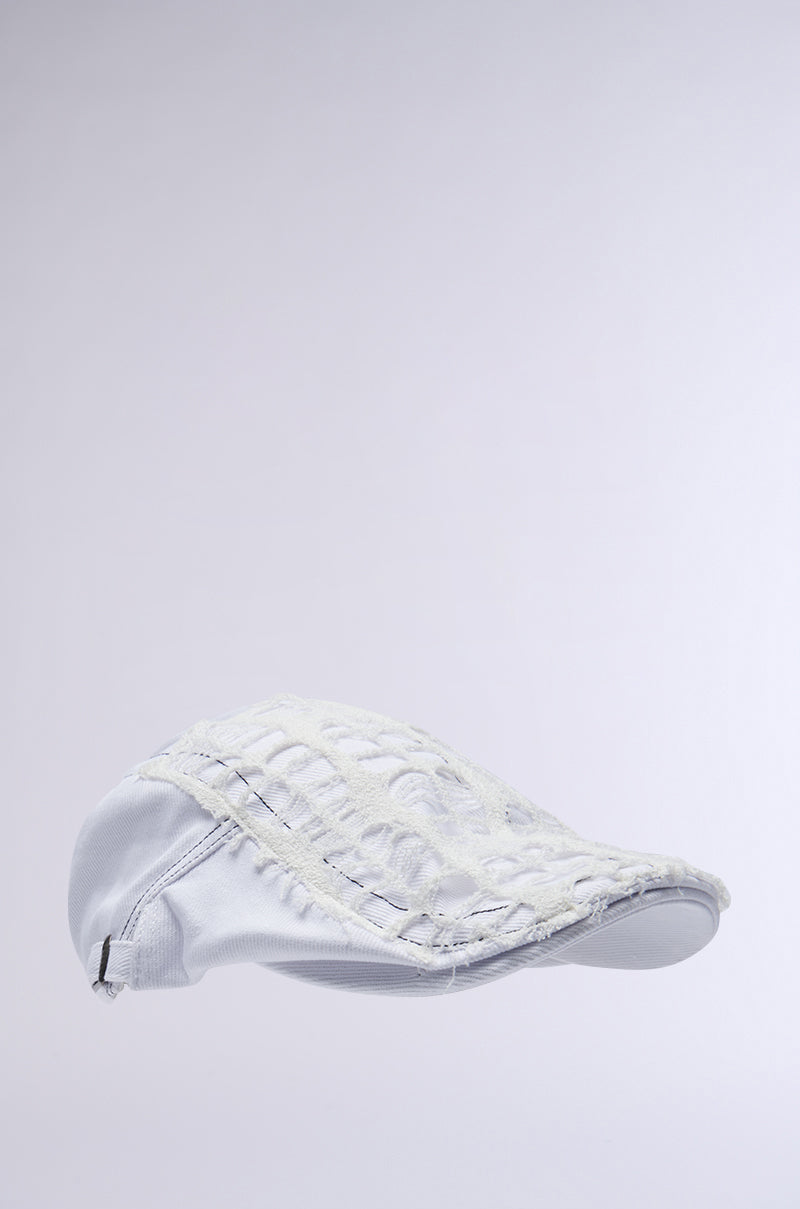 The SPREAD THE NEWS TEXTURED CAP, a white Scally cap with intricate detailing, is displayed against a light gray background. It features visible stitching, a slightly raised pattern, and an adjustable snap button for a unique and stylish look. 3