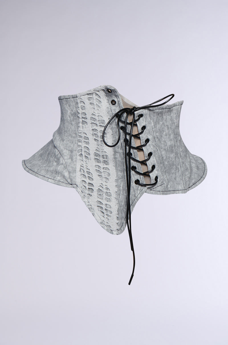 The SPREAD THE NEWS TEXTURED BELT corset, featuring a lace-up front and flared bottom with contrasting black laces, showcases an asymmetrical silhouette in gray. It has a textured belt on the left side and is set against a plain white background.
.