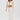 A woman wearing the PEARL HEAVEN BEADED TOP with padded shoulders and pearl embellishments, paired with wide-leg sheer pants and white pointed heels, stands against a plain white background. She has long brown hair.